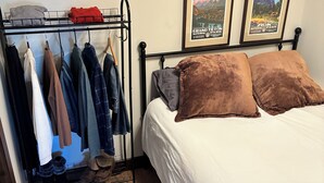 Ein Schlafzimmer mit einem Bett, einem Kleiderständer und zwei gerahmten Postern an der Wand.