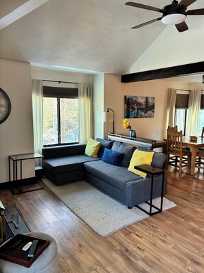 A modern living room with a sectional sofa, a dining area with a wooden table and chairs, and a ceiling fan. - Canyons Village 1 BR + Sleeping Loft/Sleeps 4/Free Ski Shuttle (Park City)