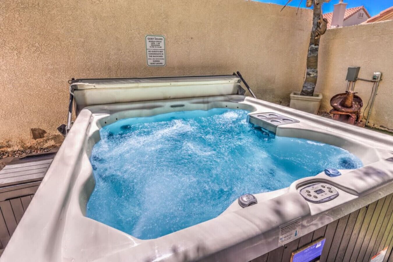 A hot tub with a control panel, surrounded by a wooden deck and a textured wall.