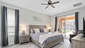 Un dormitorio con cama, mesitas de noche, ventilador de techo y un amplio ventanal con cortinas.