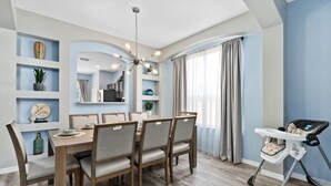 Un comedor con una mesa y sillas de madera, una trona para bebé y estantes con adornos.