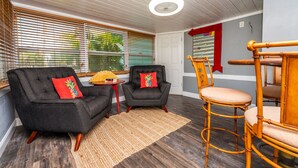 Ein gemütliches Zimmer mit einem dunkelgrauen Sofa, zwei Sesseln, einem Holzstuhl und einem kleinen Tisch mit einer Ananas-Dekoration.