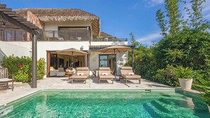 Eine moderne Villa mit Swimmingpool, Sitzgelegenheiten im Freien und einem Reetdach.