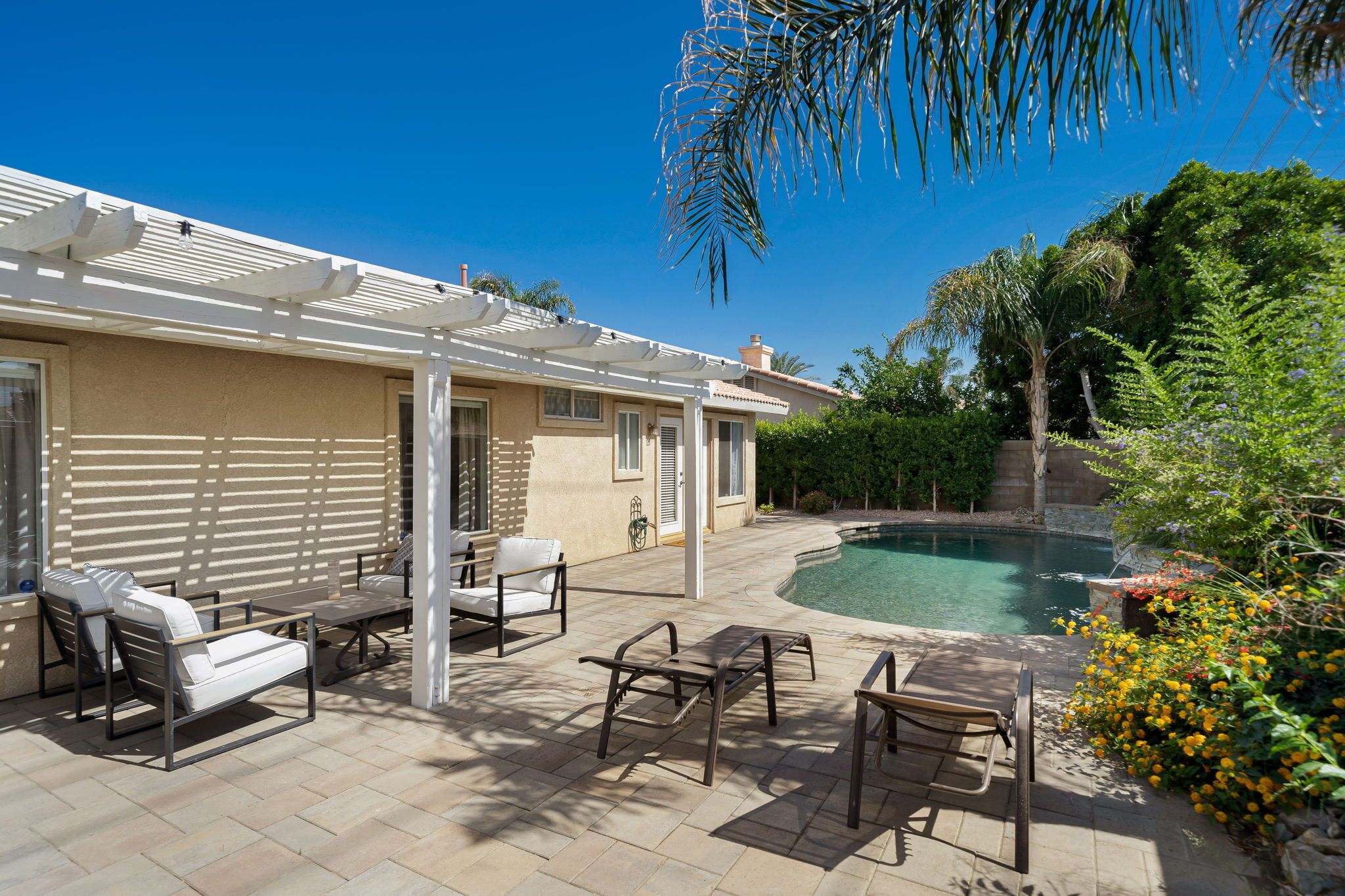 A patio area with outdoor furniture, a pool, and lush greenery.