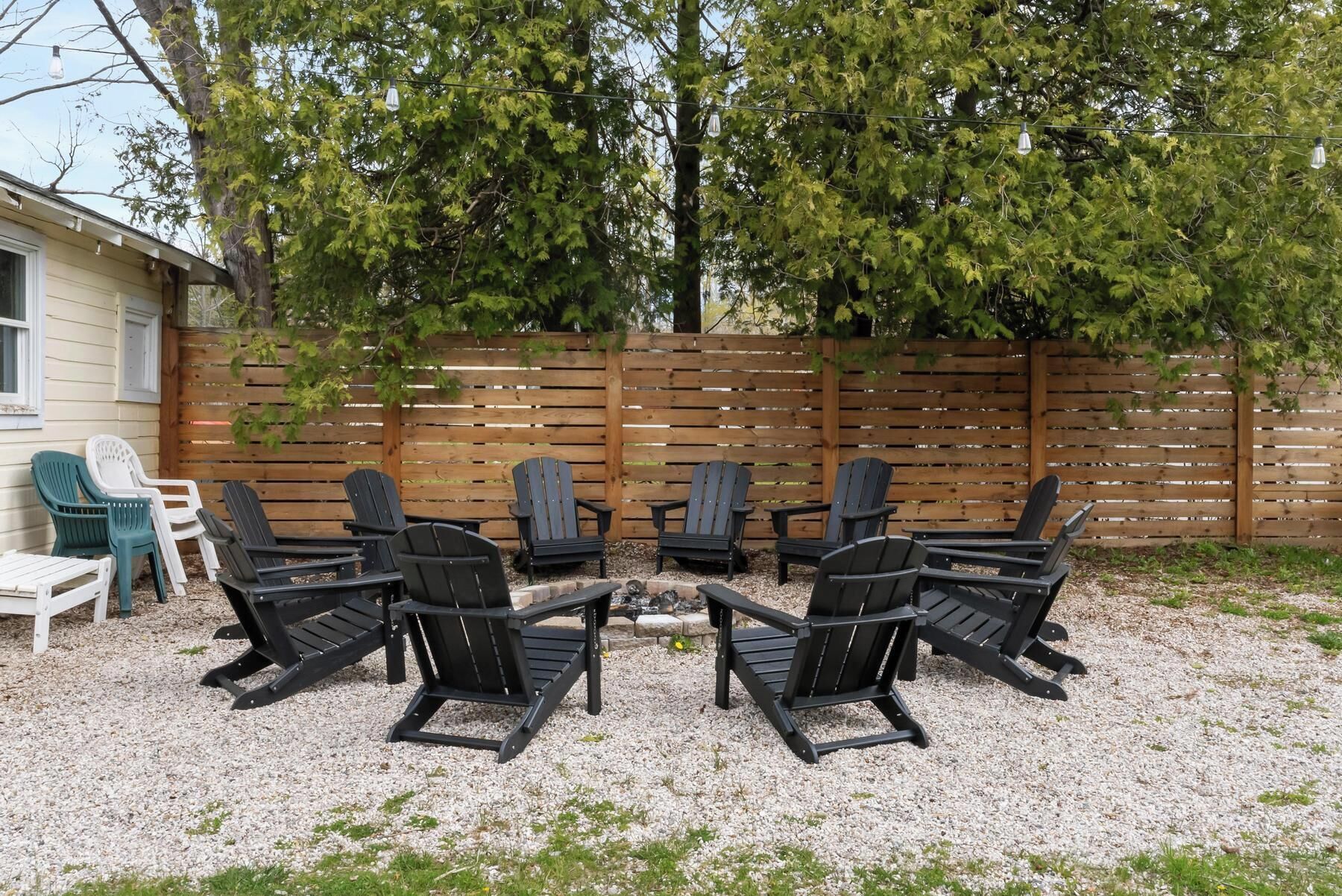 Een achtertuin met een houten omheining, een vuurkorf en diverse Adirondack-stoelen eromheen.