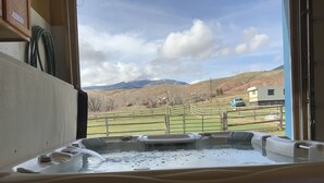 A hot tub with a view of a fenced pasture and distant mountains.
