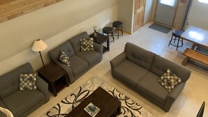 A spacious living area with two sofas, a coffee table, and a lamp. There is a door leading to another room and a window with blinds.