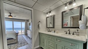 A bathroom with a large mirror, a green vanity, and a view of the ocean.