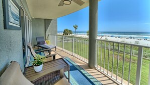 A balcony with a view of the beach, a ceiling fan, and outdoor furniture.