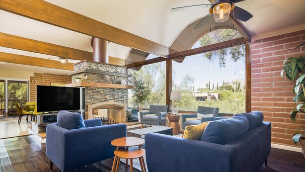 A spacious living room with a stone fireplace, blue sofas, and a large TV. - Casa Velo -Mid Century Hot Tub & Amazing Backyard (Tucson)