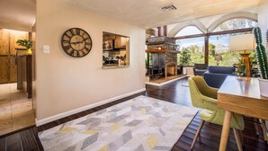 A spacious living area with a fireplace, a clock, and a view of the outdoors. - Casa Velo -Mid Century Hot Tub & Amazing Backyard (Tucson)