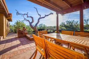 An outdoor patio with a wooden table and chairs, a tree, and a view of the surrounding landscape.