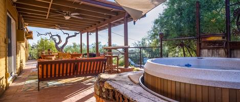 Un espacio al aire libre techado con un jacuzzi, bancos de madera y una mesa de patio.
