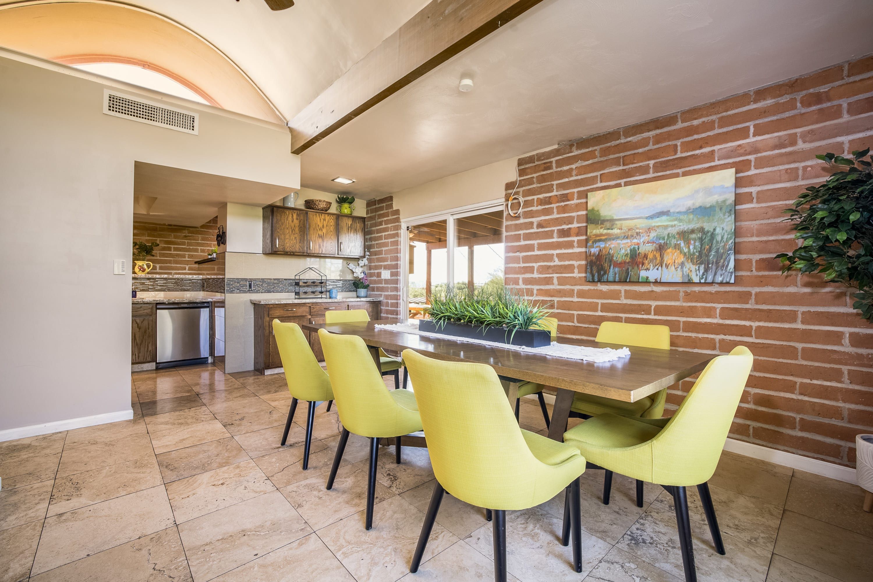 A dining area with a brick wall, a painting, and a table with chairs.