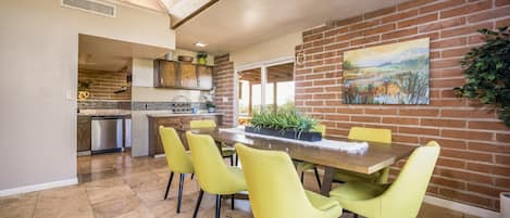 A dining area with a brick wall, a painting, and a table with chairs.