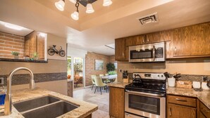 A modern kitchen with granite countertops, stainless steel appliances, and wooden cabinets. - Casa Velo -Mid Century Hot Tub & Amazing Backyard (Tucson)