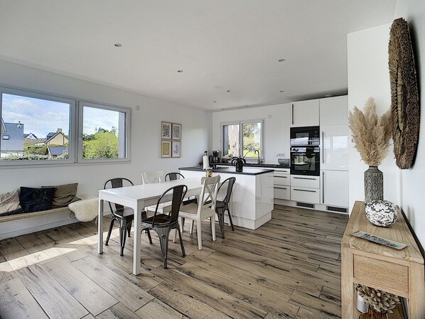 A modern kitchen with white cabinets, a central island, and a dining area with a white table and chairs.