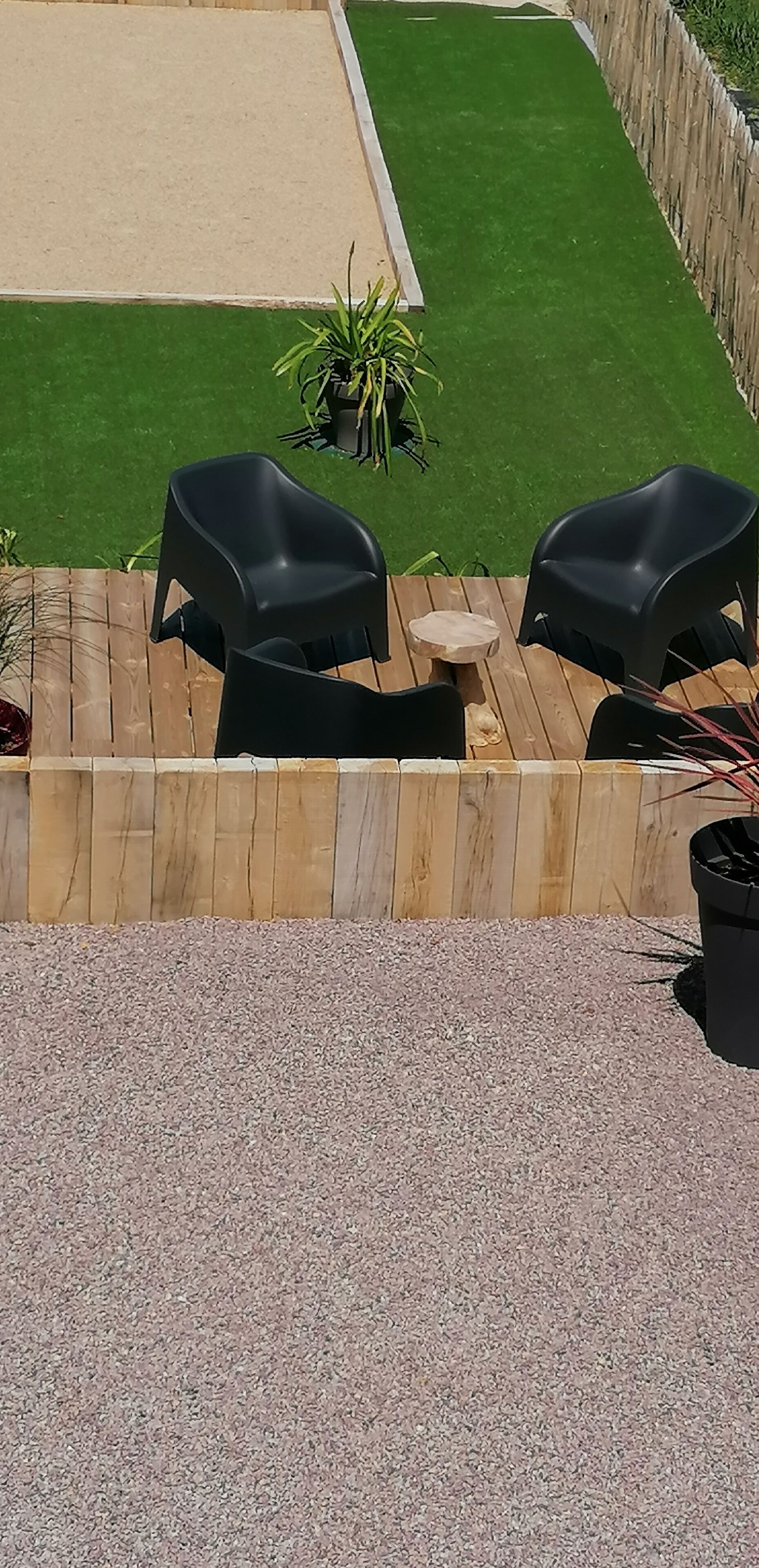 Een terras met twee zwarte plastic stoelen, een klein rond tafeltje en een bloempot.