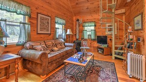A cozy cabin interior with a wooden interior, a sofa, a coffee table, a television, and a spiral staircase. - Cross Creek Ranch located near Lake Watauga and Mountain City (Mountain City)