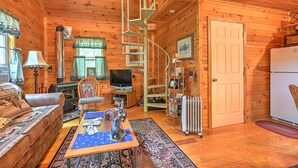 A cozy cabin interior with a wooden interior, a spiral staircase, a television, a fireplace, and a refrigerator. - Cross Creek Ranch located near Lake Watauga and Mountain City (Mountain City)