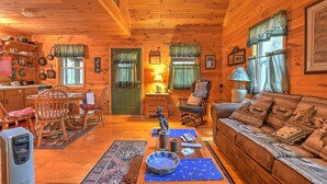 A cozy log cabin interior with a dining area, a sofa, and a fireplace. - Cross Creek Ranch located near Lake Watauga and Mountain City (Mountain City)