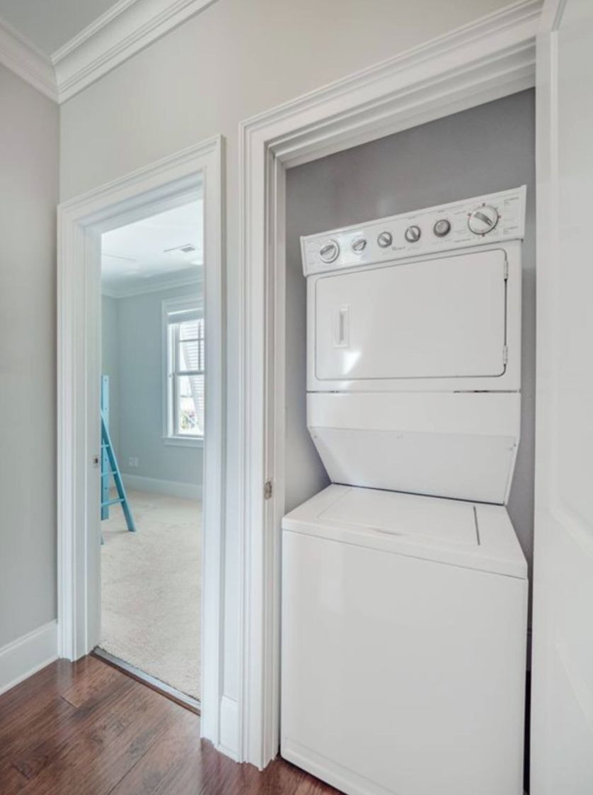 A laundry room with a stacked washer and dryer, a wooden floor, and a door leading to a balcony.