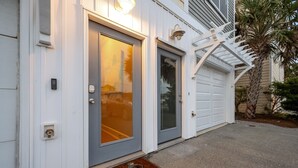Une maison avec une porte grise, une porte de garage et un paillasson orné d’un symbole de vélo.