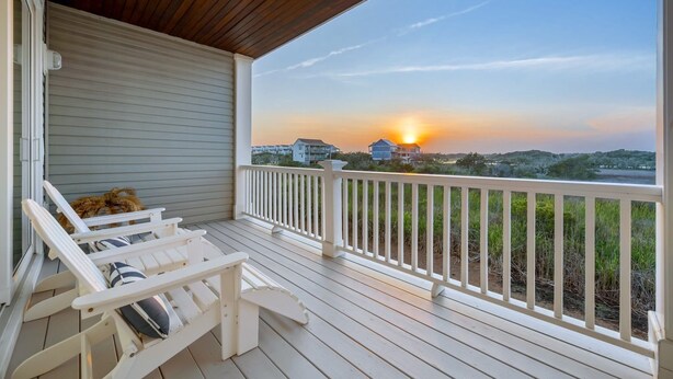 Une véranda couverte avec des balustrades blanches et deux fauteuils Adirondack blancs.
