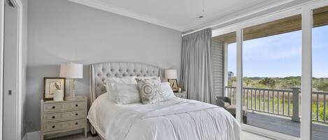 A bedroom with a large bed, a ceiling fan, a nightstand with lamps, and a view of the outdoors through a sliding glass door.