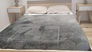 Un lit avec une couverture grise, deux tables de chevet avec des lampes et une tête de lit en bois.
