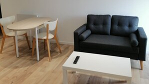 Un salon moderne avec un canapé noir, une table basse blanche et un coin repas comprenant une table blanche et des chaises en bois.