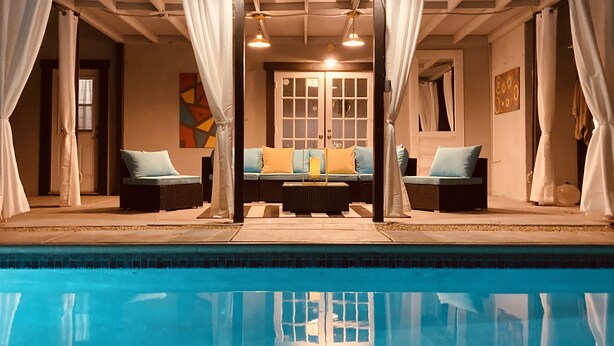A poolside area with a seating arrangement, a covered section with a door, and a view of the pool.