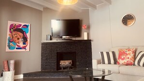 A living room with a fireplace, a television on a stand, a sofa with patterned cushions, and a painting on the wall.