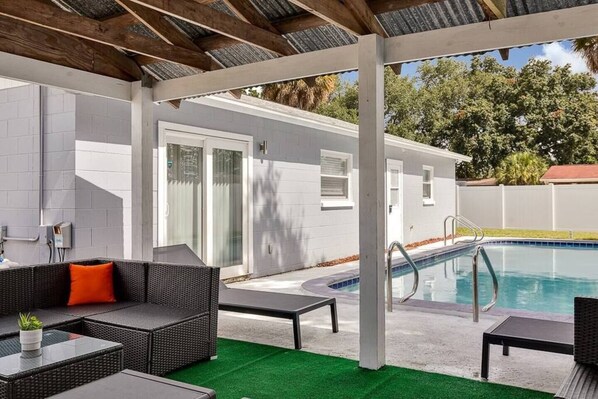 An outdoor pool area with a covered patio, lounge chairs, and a small table. - Heated Pool & Game Room, Sleeps 14 | 10 Min to Tampa Airport & Stadium (Tampa)