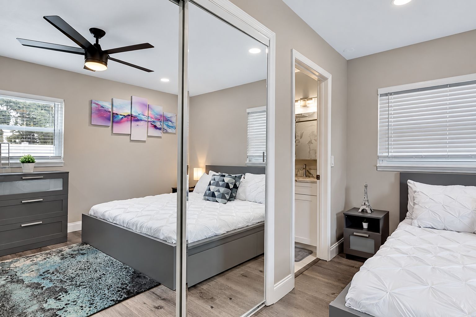 A modern bedroom with a bed, bedside tables, a dresser, a ceiling fan, and a large mirror.