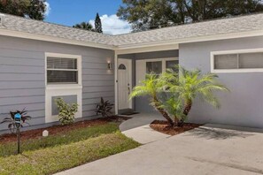 A single-story house with a front porch, a small garden with palm trees, and a mailbox. - Heated Pool & Game Room, Sleeps 14 | 10 Min to Tampa Airport & Stadium (Tampa)