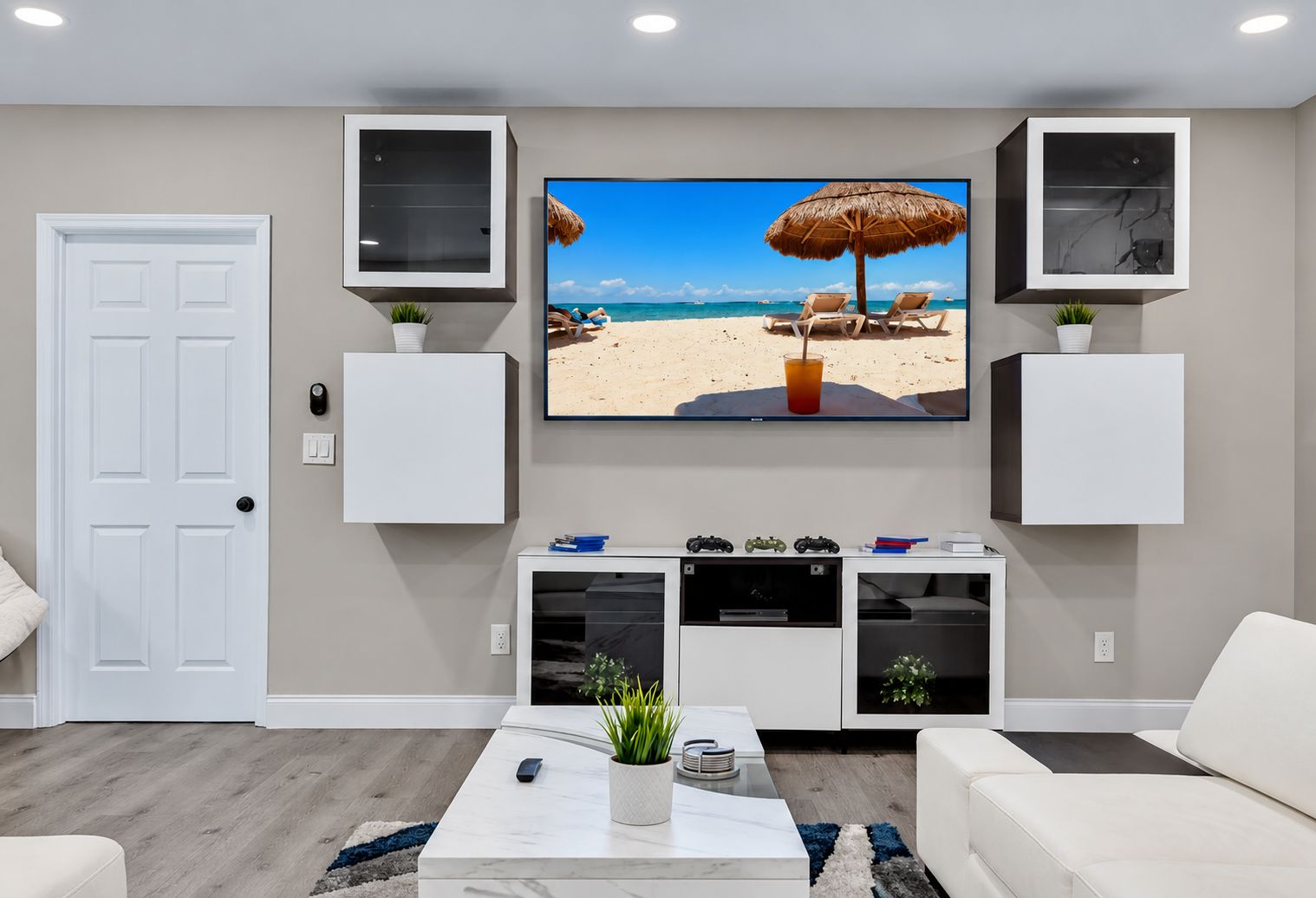 Una sala de estar con un televisor de pantalla plana sobre un mueble blanco, una puerta y un sofá blanco.