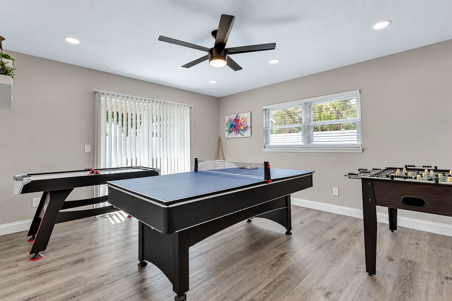 Une pièce équipée d’une table de ping-pong, d’un baby-foot et d’un ventilateur de plafond.