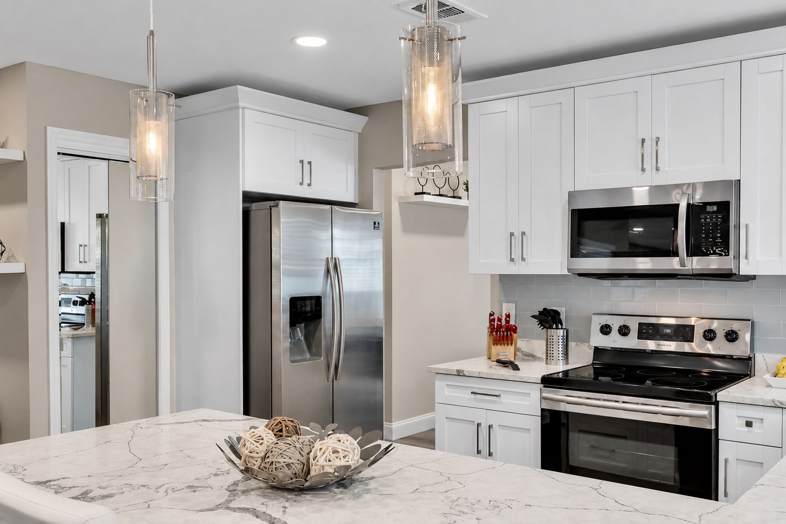 A modern kitchen with stainless steel appliances, white cabinetry, and a marble countertop.