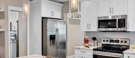 A modern kitchen with stainless steel appliances, white cabinetry, and a marble countertop.