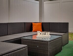 A dark wicker sectional sofa with an orange cushion and a glass coffee table with 'RELAX' on it. - Heated Pool & Game Room, Sleeps 14 | 10 Min to Tampa Airport & Stadium (Tampa)