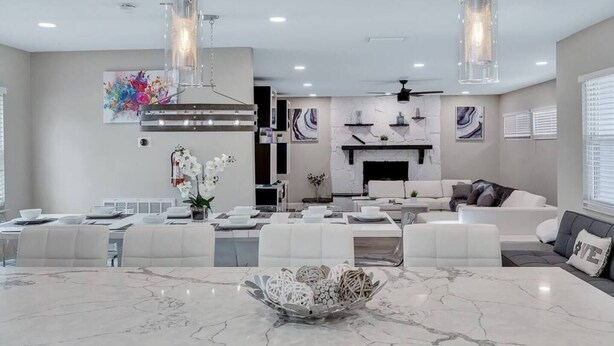 A modern living room with a fireplace, a dining area with a marble table, and a ceiling fan. - Heated Pool & Game Room, Sleeps 14 | 10 Min to Tampa Airport & Stadium (Tampa)