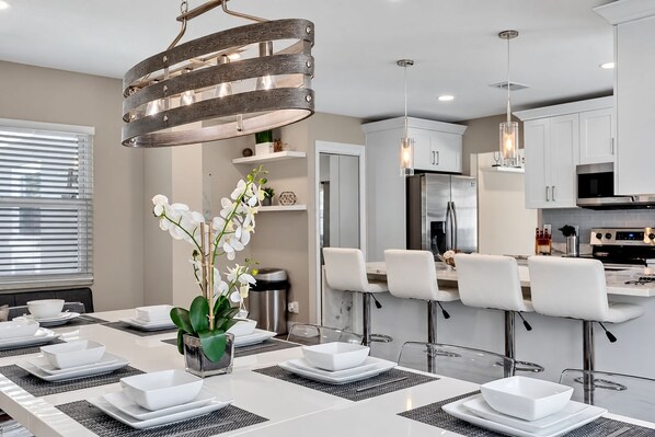 A modern kitchen with white cabinetry, stainless steel appliances, and a dining area with a long table and bar stools.