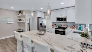 A modern kitchen with white cabinets, stainless steel appliances, and a marble countertop. - Heated Pool & Game Room, Sleeps 14 | 10 Min to Tampa Airport & Stadium (Tampa)