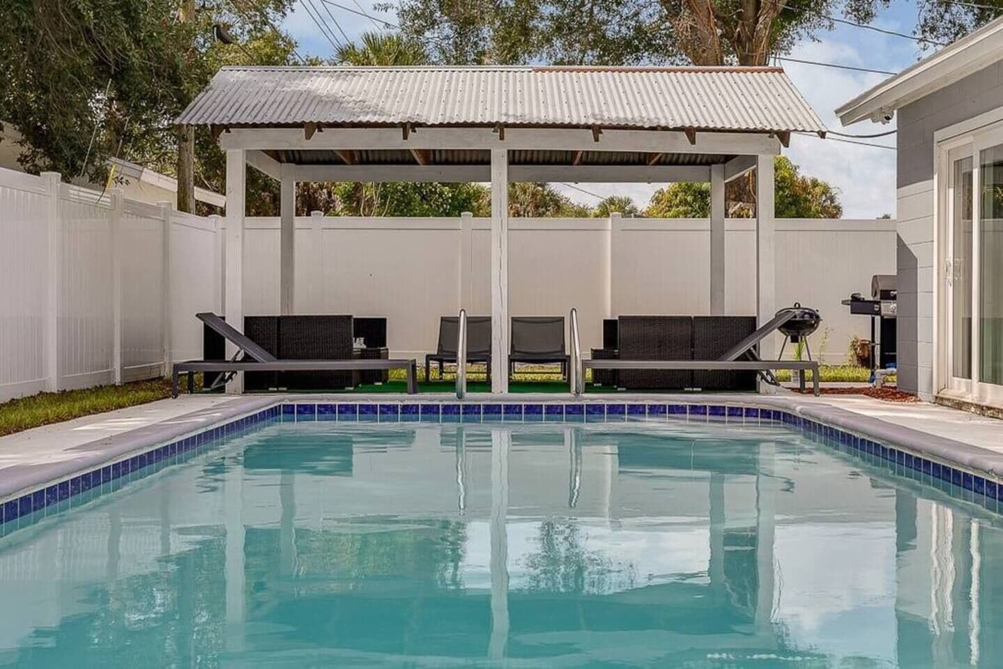 Una piscina con sillones de descanso y un área de estar techada.