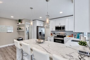 A modern kitchen with white cabinets, stainless steel appliances, a marble island, and pendant lighting.