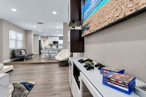A modern living room with a gaming setup, a sofa, and a dining area in the background.