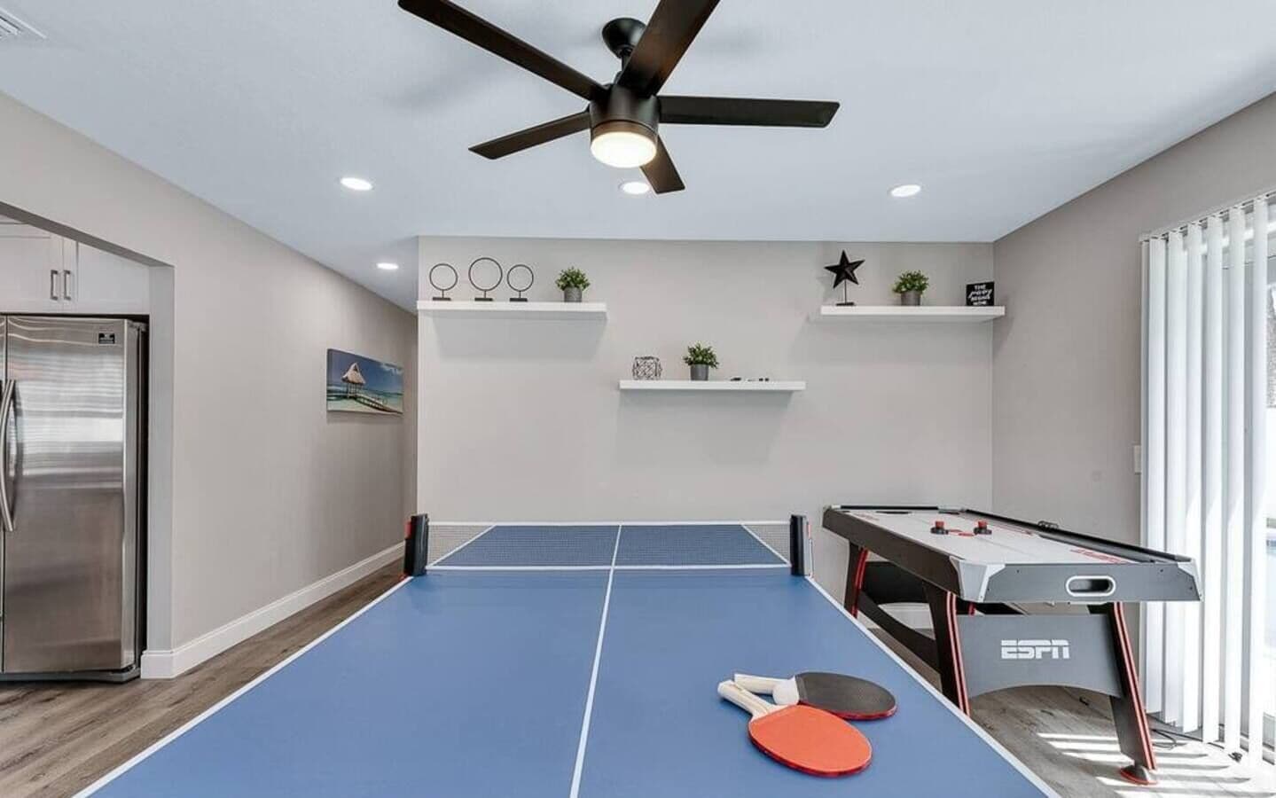 A room with a ping pong table, a foosball table, and a ceiling fan.