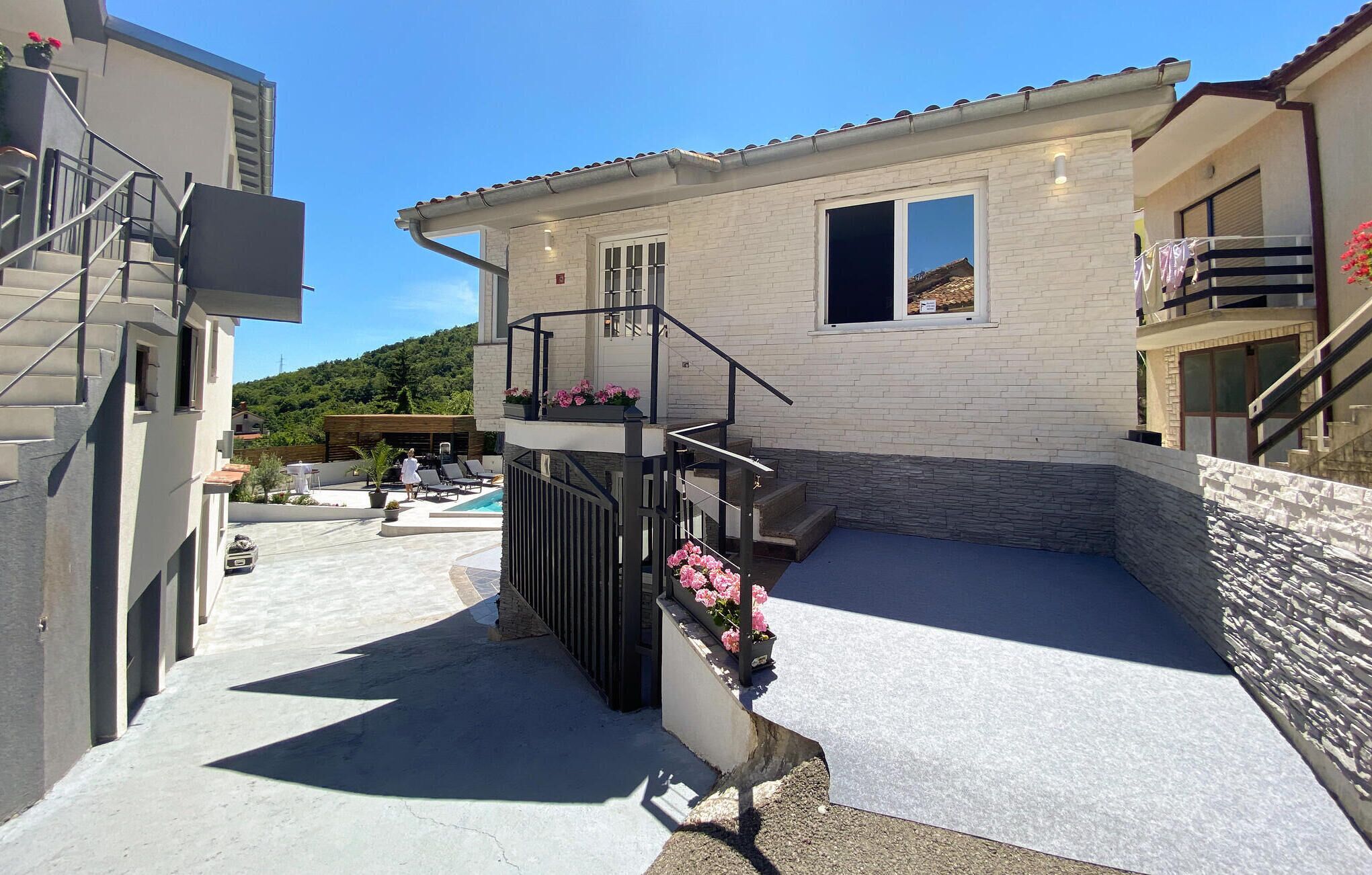 A modern house with a pool, a balcony with flowers, and a staircase leading to the upper floor.