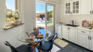 A modern kitchen with a glass dining table, white cabinets, and a view of an outdoor pool. - Amazing home in Rukavac (Rukavac)